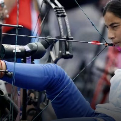 a woman sits in a chair and draws a bow with her foot and mouth